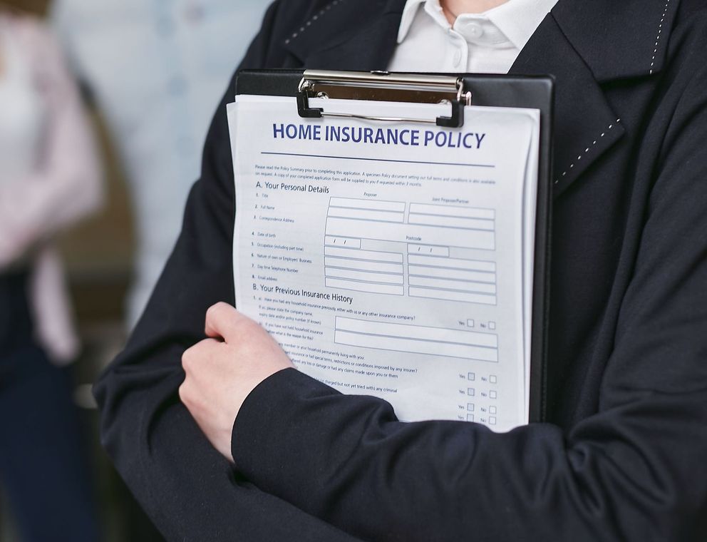 Person holding a clipboard labeled “Home Insurance Policy” with a document form visible
