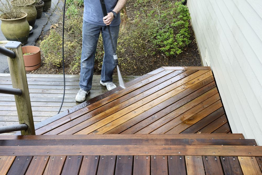 A Man Is Cleaning A Wooden Deck With Pressure Washer — Jervis Bay Pressure Washing & Property Maintenance In Vincentia, NSW