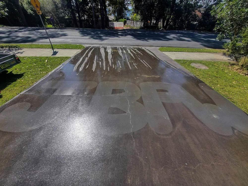 A Concrete Driveway Is Being Cleaned With A Hose — Jervis Bay Pressure Washing & Property Maintenance in Sanctuary Point, NSW