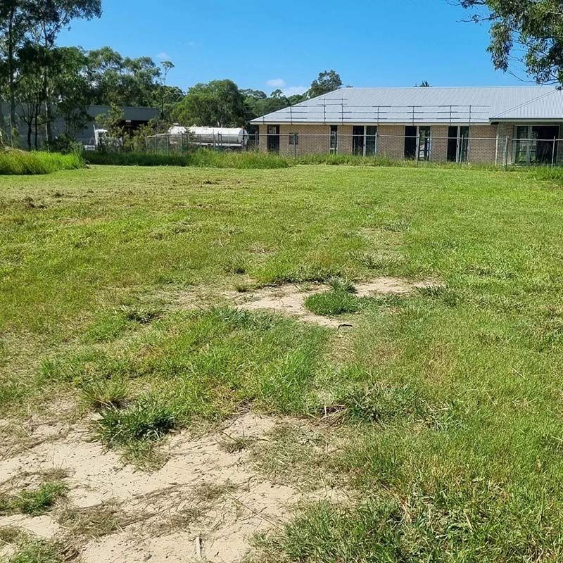 A Large Grassy Field With A House In The Background — Jervis Bay Pressure Washing & Property Maintenance in Sussex Inlet, NSW