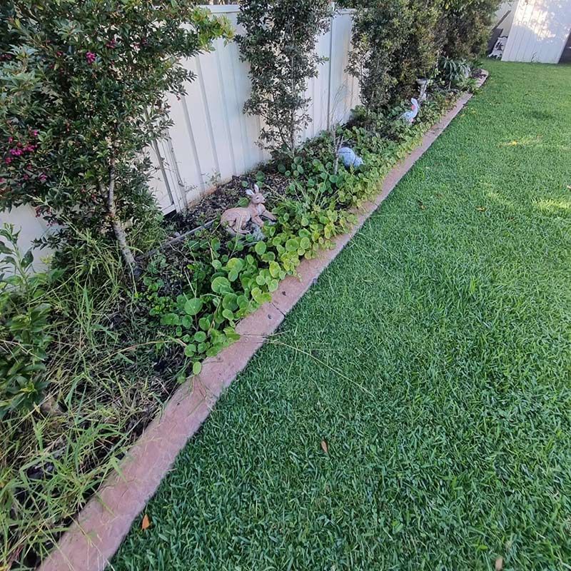 A Lush Green Yard With A White Fence And A Brick Curb — Jervis Bay Pressure Washing & Property Maintenance In Berry, NSW
