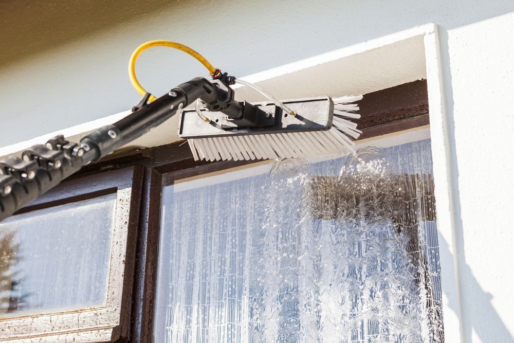 A Person Is Cleaning A Window With A Brush — Jervis Bay Pressure Washing & Property Maintenance In Sanctuary Point, NSW