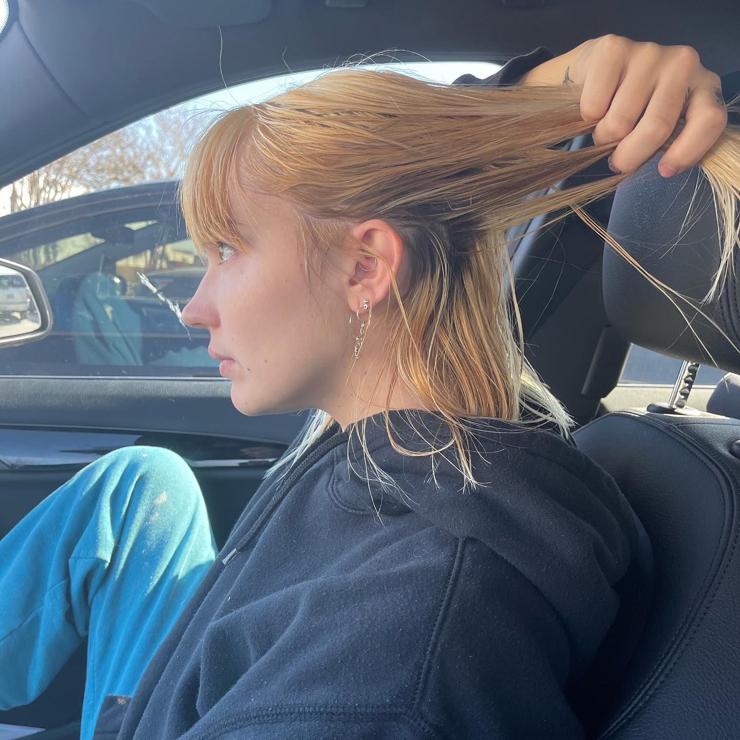 Person sitting in a car, pulling back long red hair in the sunlight