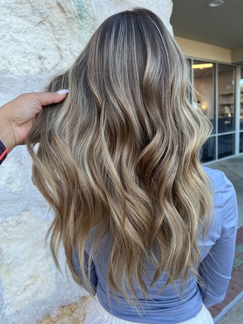 Woman with long wavy hair, highlighted with blonde and brown tones, being styled.