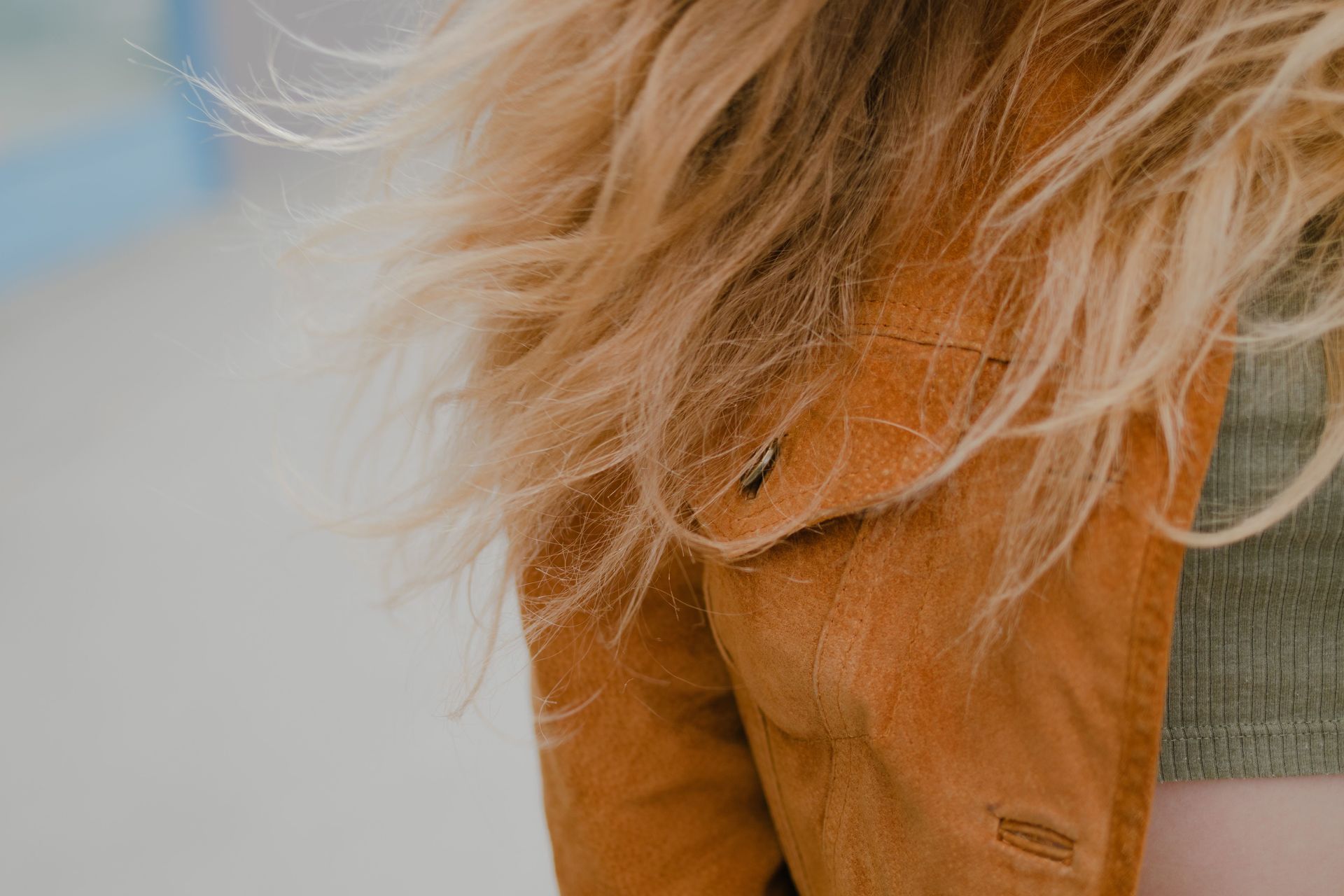 Close-up of a tan leather jacket with light brown hair and a gray sweater visible
