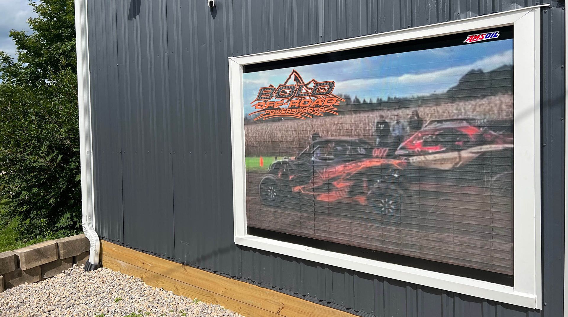 Large framed photo of a red race car on a dark gray exterior wall with gravel below