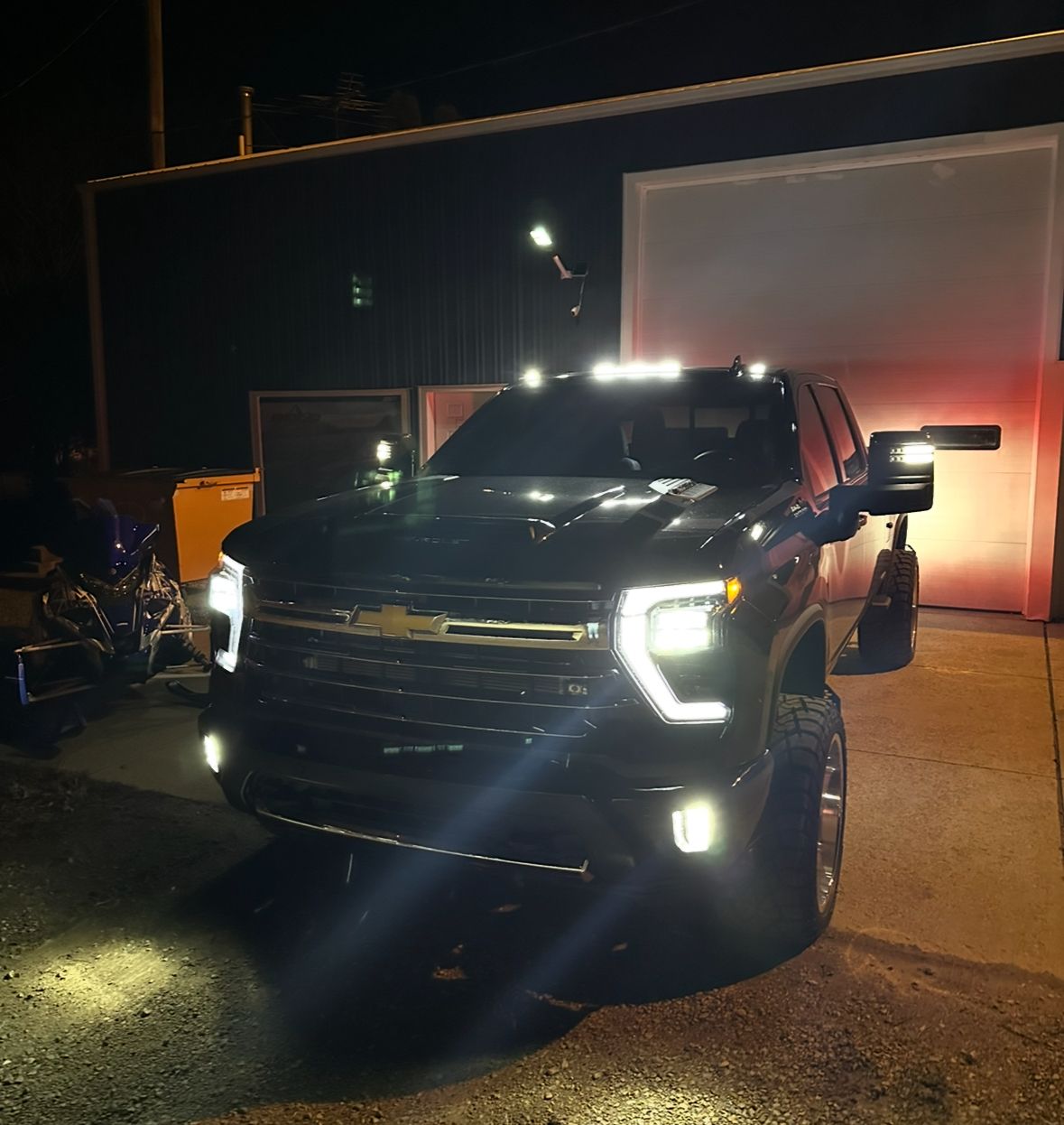 Black pickup truck with bright headlights parked at night outside a building with an open door
