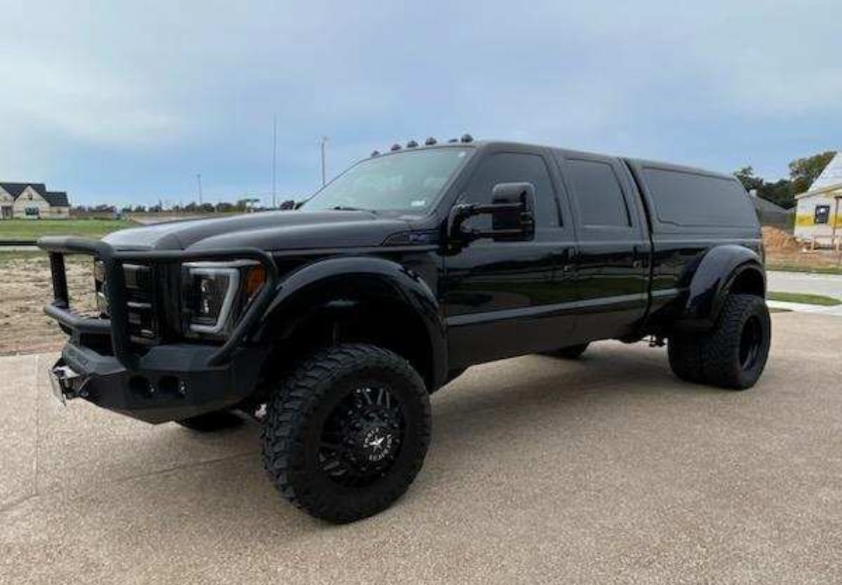 Black lifted pickup truck parked outdoors on a paved lot under a cloudy sky