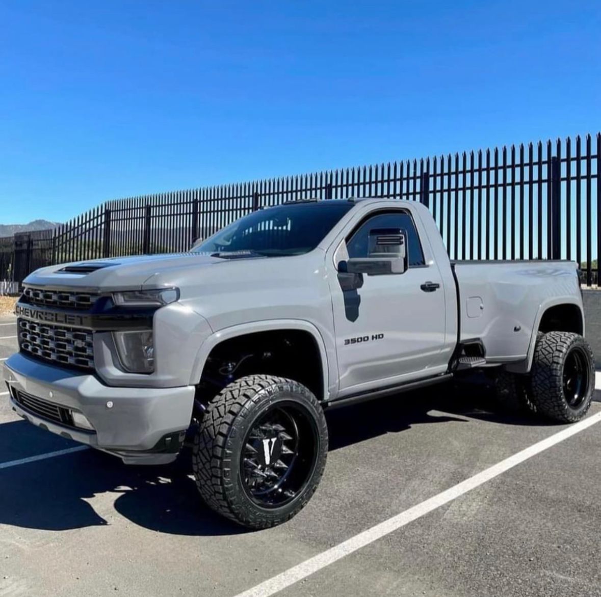 White lifted GMC pickup truck parked beside a fence on a sunny day