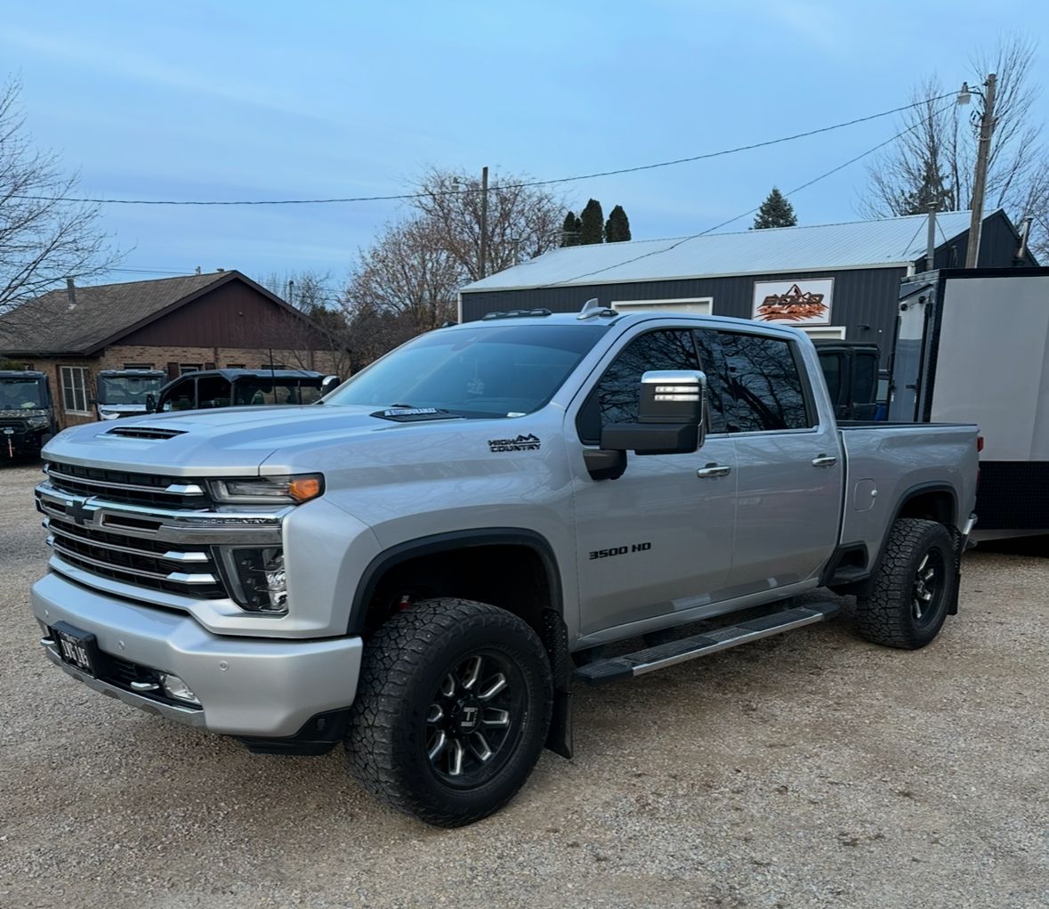 Silver pickup truck parked outdoors beside a building on a gravel lot.