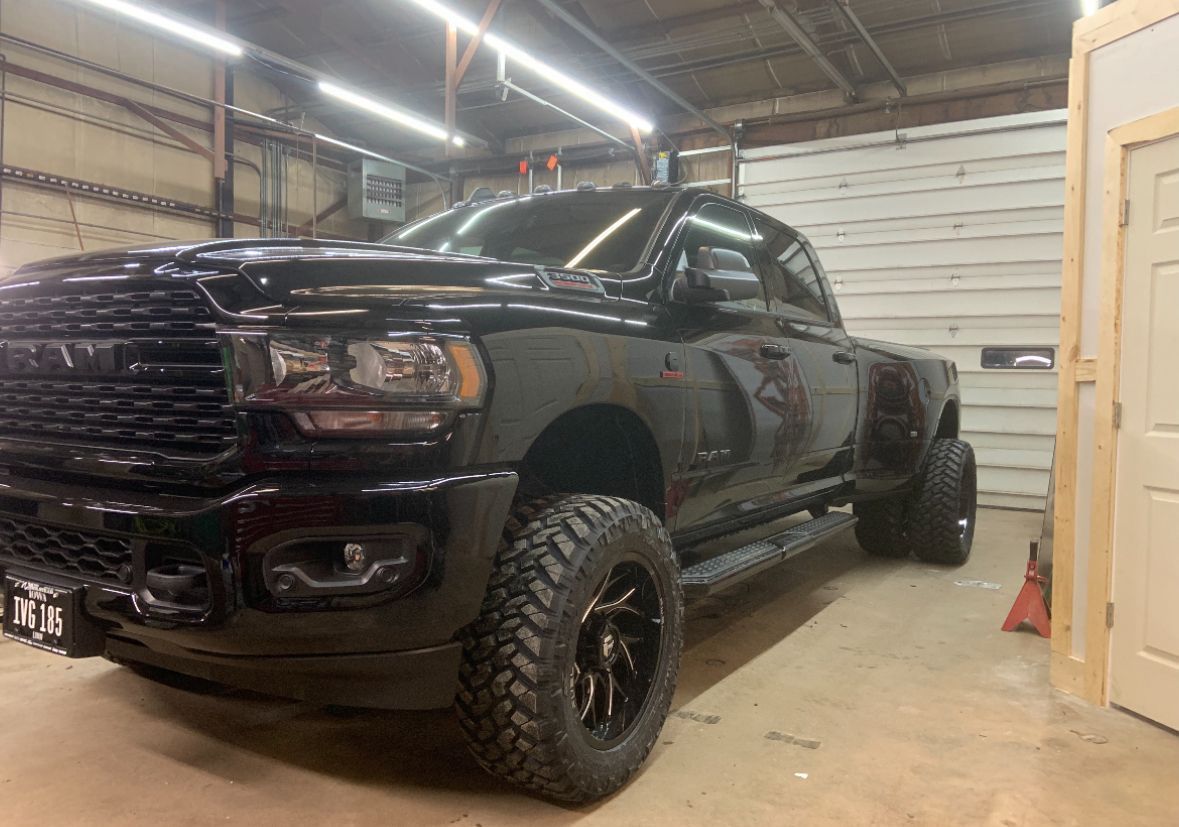 Black lifted pickup truck parked in a garage, viewed from the front-left side.