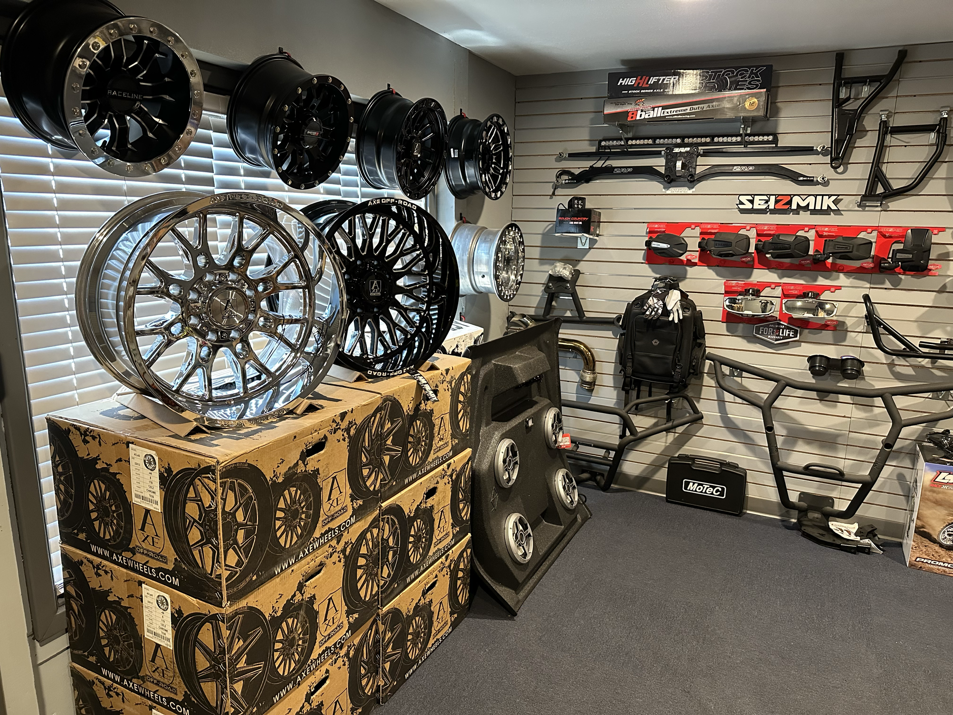 Tire and wheel shop with display shelves of rims, tires, and automotive parts on walls and boxes.