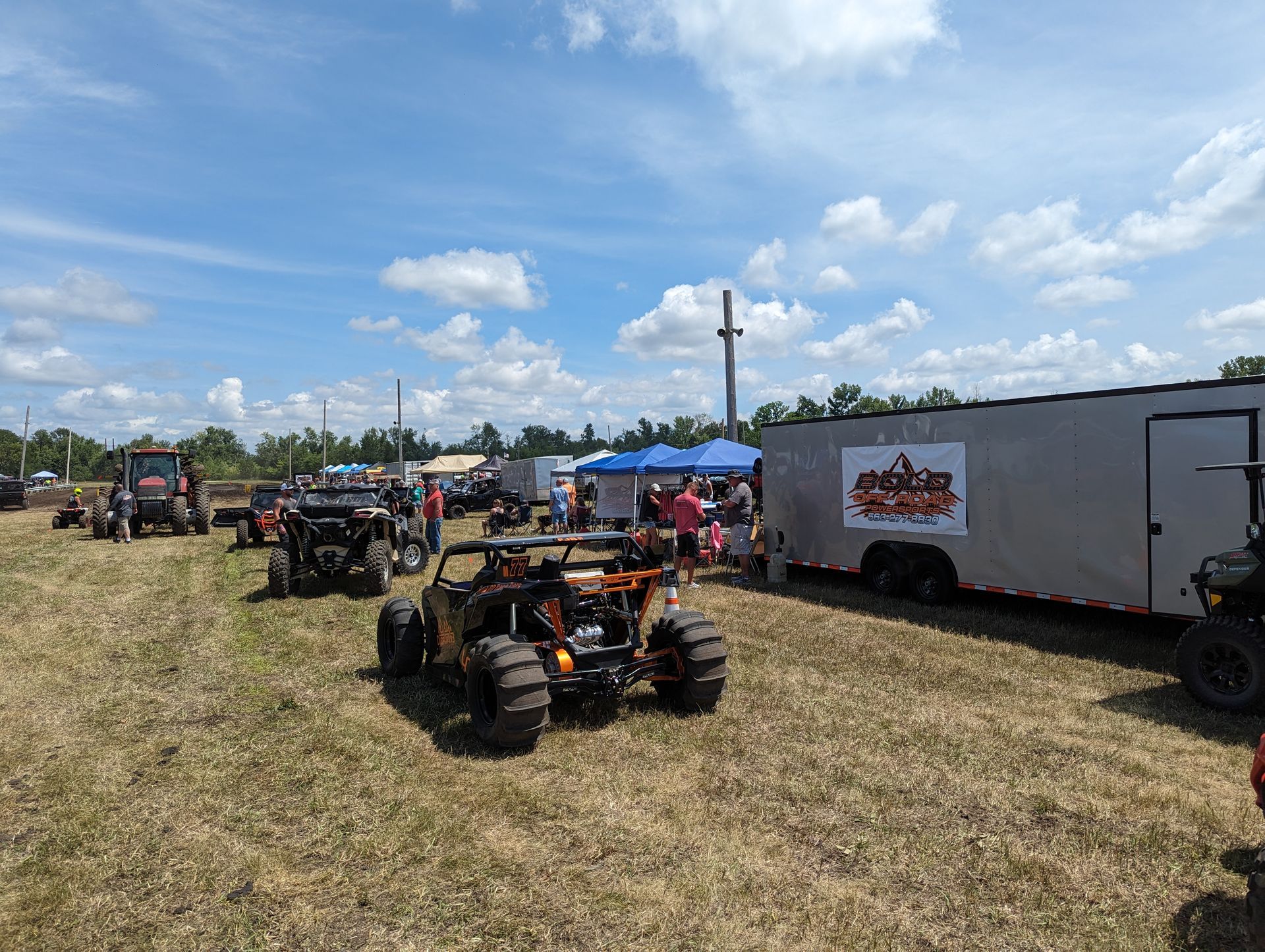 ATVs lined up on a grassy field beside a white trailer under a blue sky