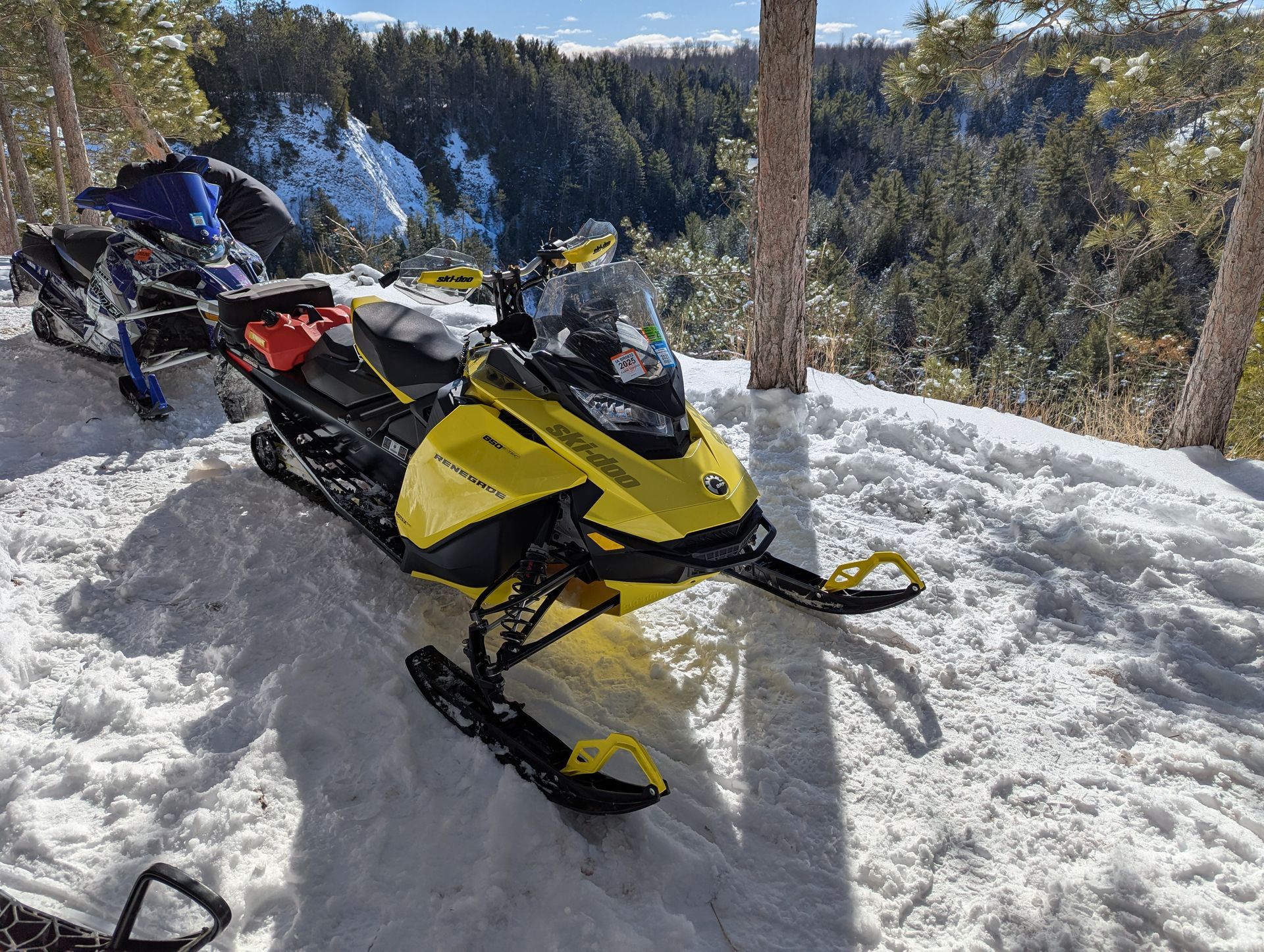 Yellow snowmobile parked on snowy trail with forested mountains in the background