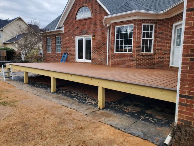 Raised wooden deck attached to a brick house under construction in a backyard