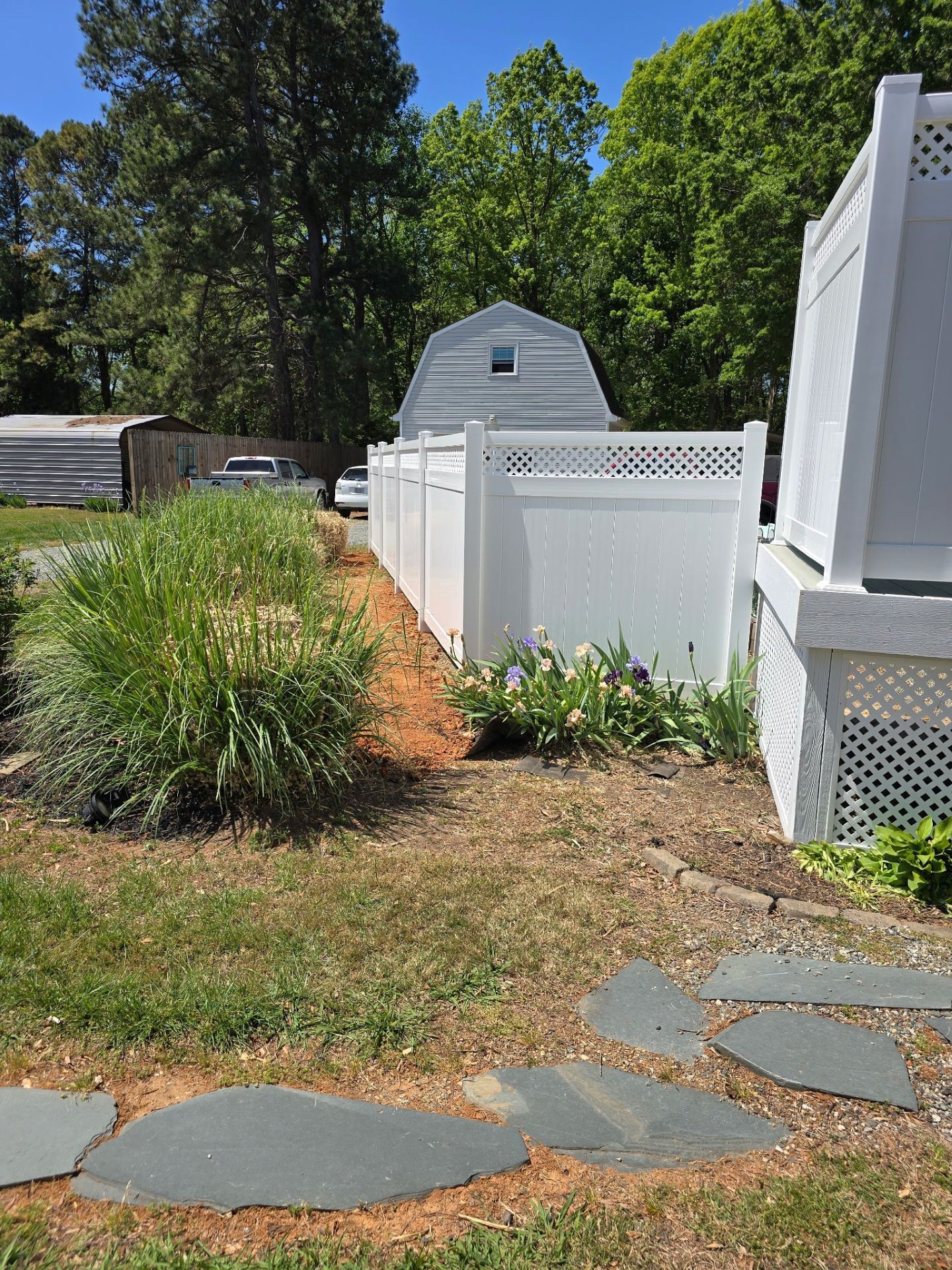 Backyard with white vinyl fence, stone path, and small shed amid trees and grass