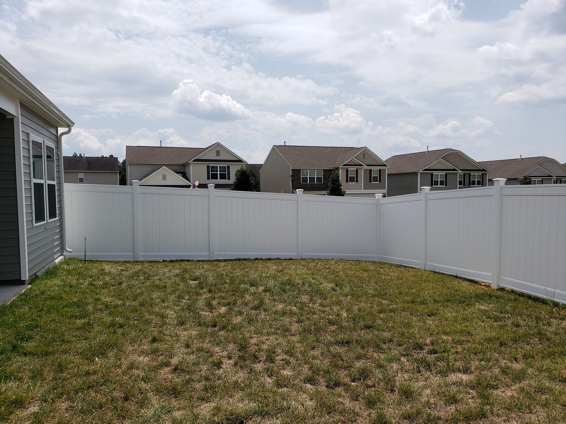 Small fenced backyard with patchy grass under a cloudy sky, viewed from a patio.