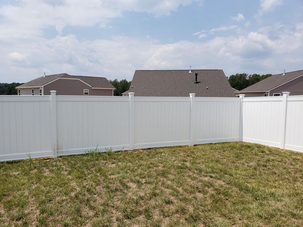 White vinyl fence enclosing a grassy backyard with neighboring rooftops under a partly cloudy sky