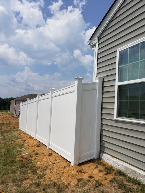 White vinyl fence along the side of a gray house under a cloudy sky