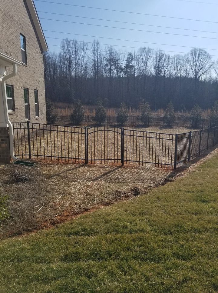 Brick house beside a black metal fence in a grassy yard with bare trees beyond