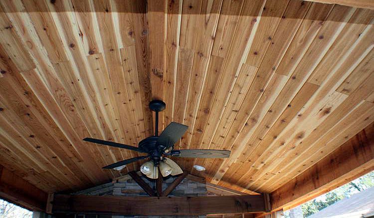 A ceiling covered in light-brown wood planks with a dark ceiling fan and light fixture hanging from the center.