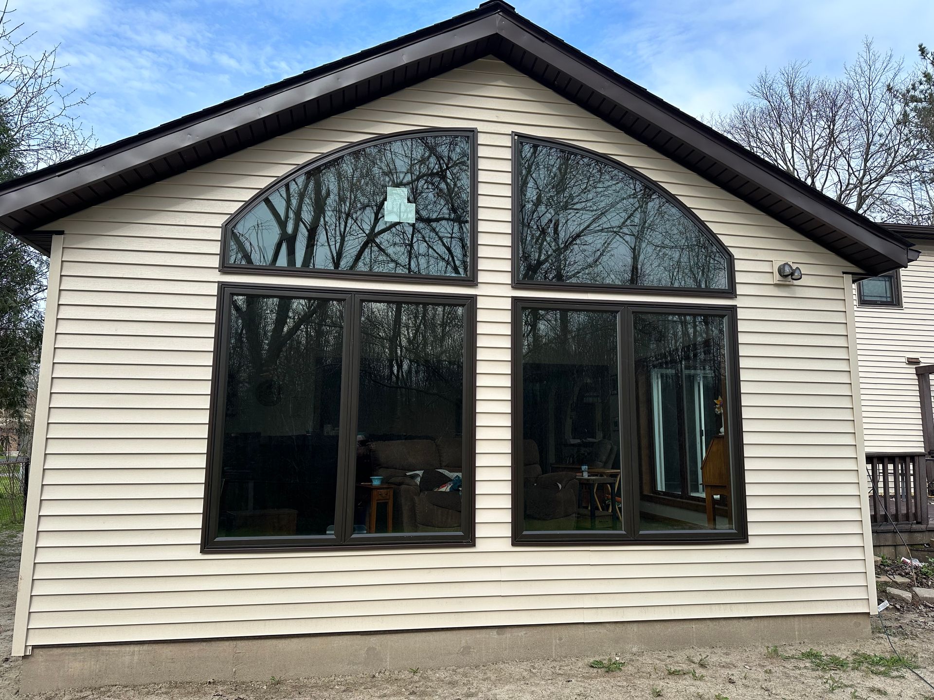 A tan-sided house exterior featuring two large, arched windows with dark brown frames under a gabled roof.