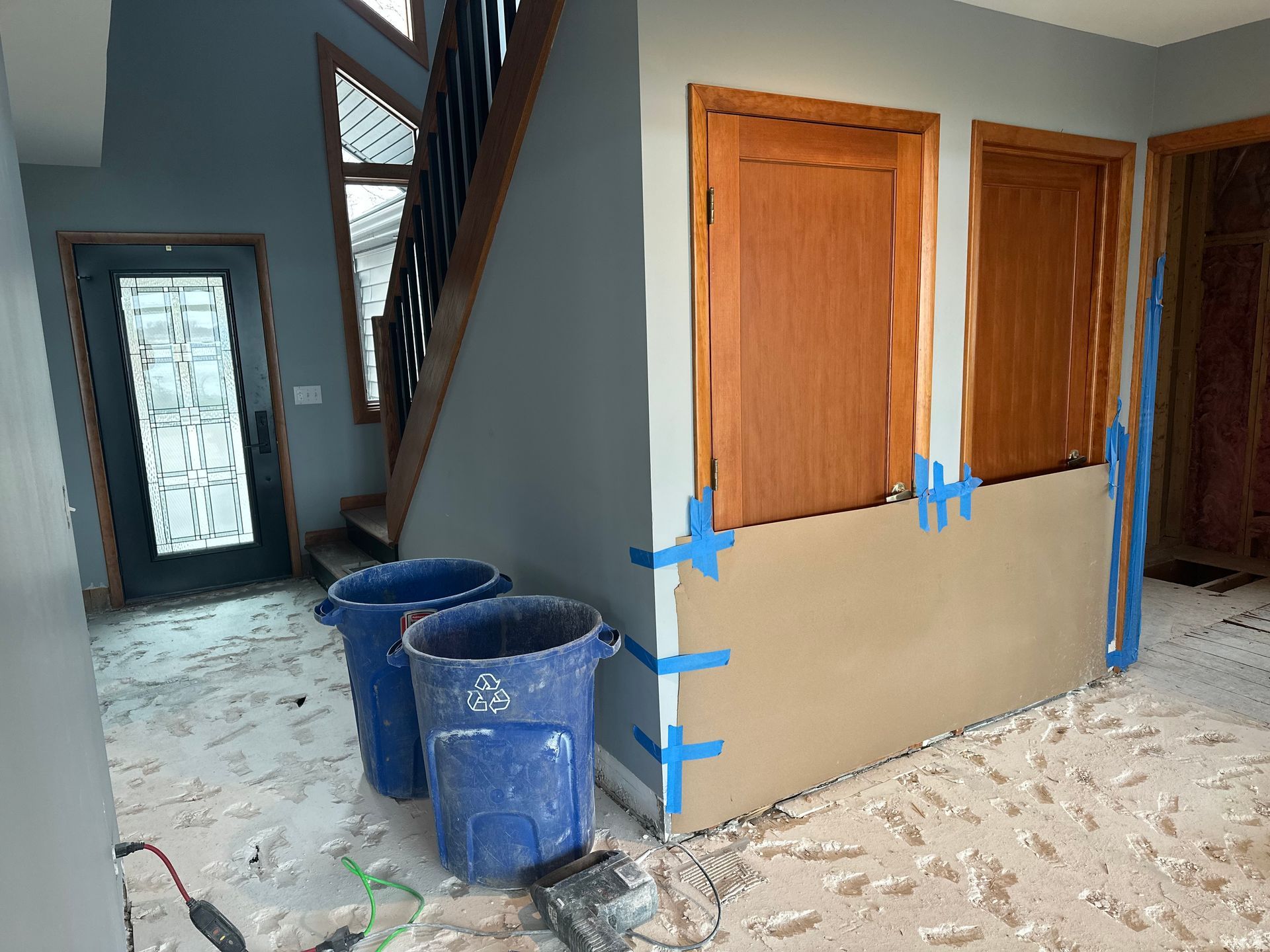 Interior view of a home under renovation with unfinished drywall walls, blue painter's tape, and two blue trash bins.