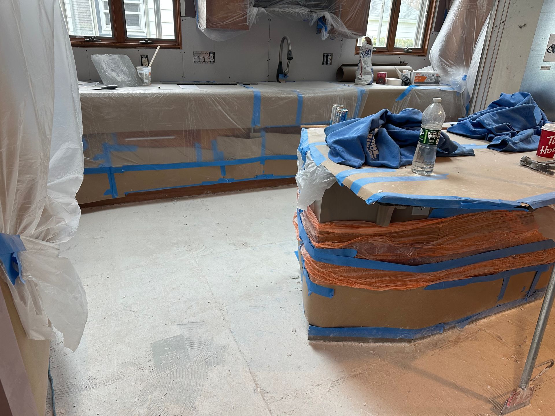 A kitchen under construction with paper-covered countertops and floor, protected by blue painter's tape.