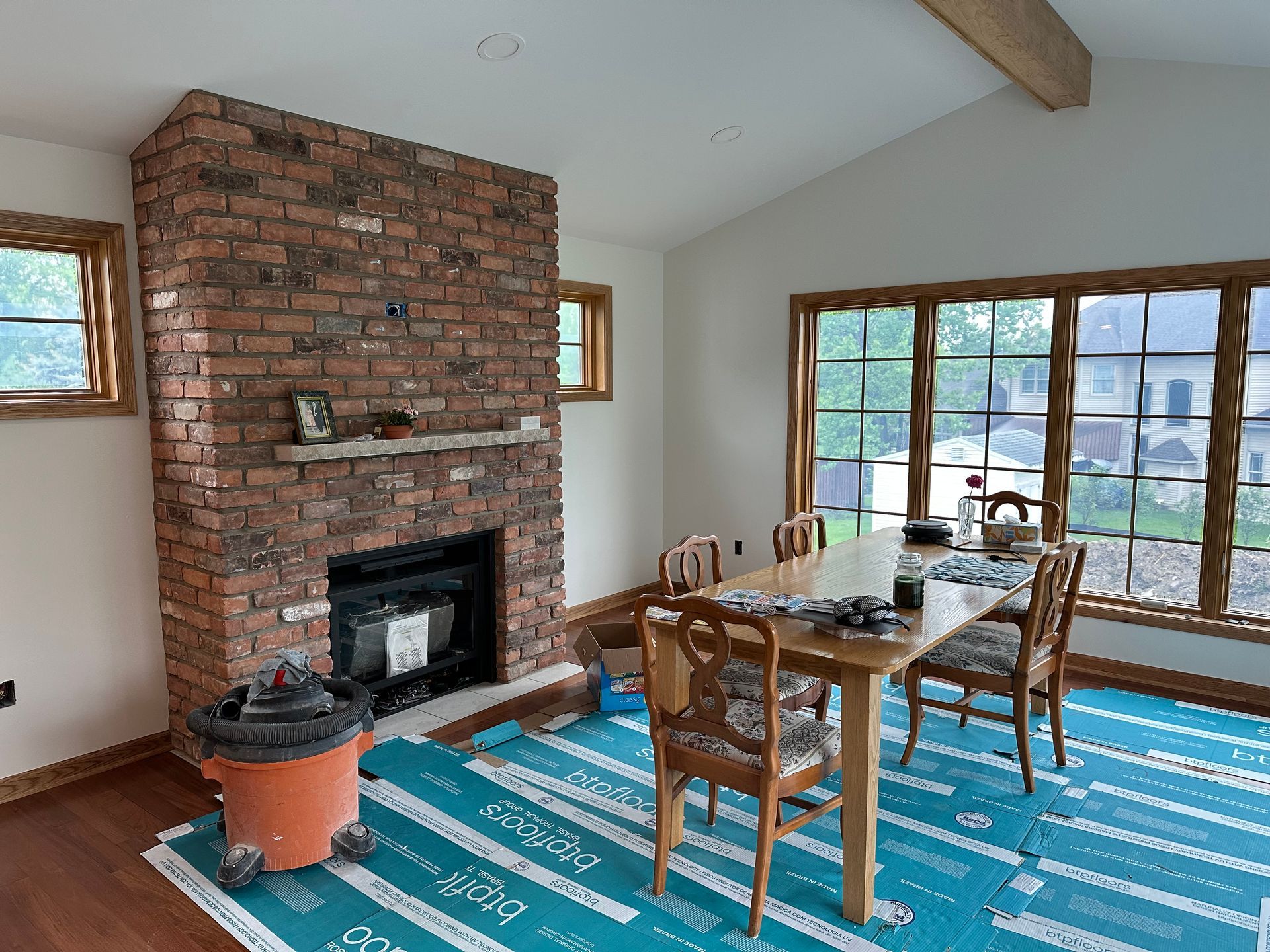 Dining area with a brick fireplace, wooden table, and chairs, set on a blue protective floor covering.