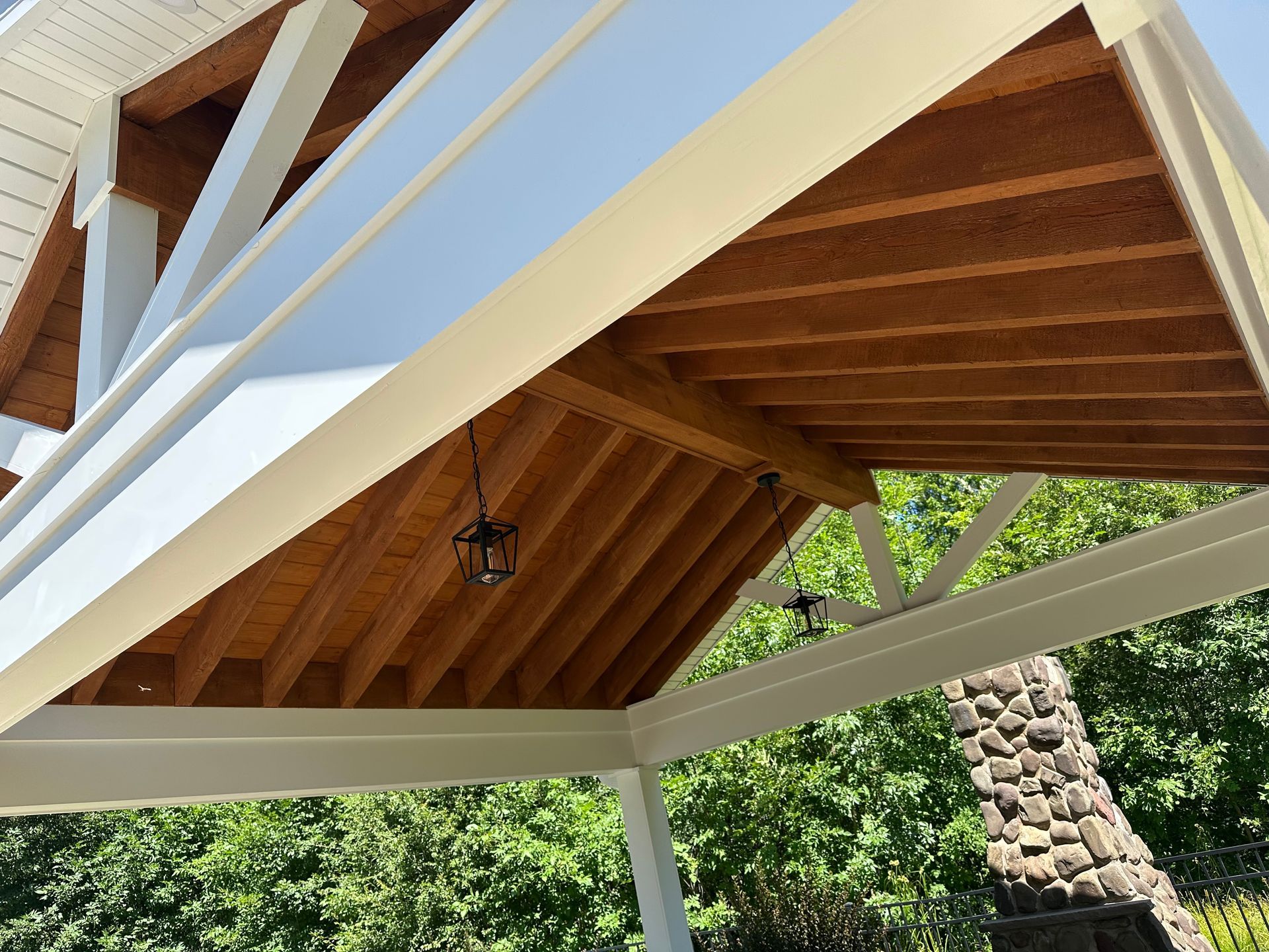 An outdoor wooden pavilion with a peaked roof, exposed timber beams, hanging lanterns, and a stone chimney nearby.