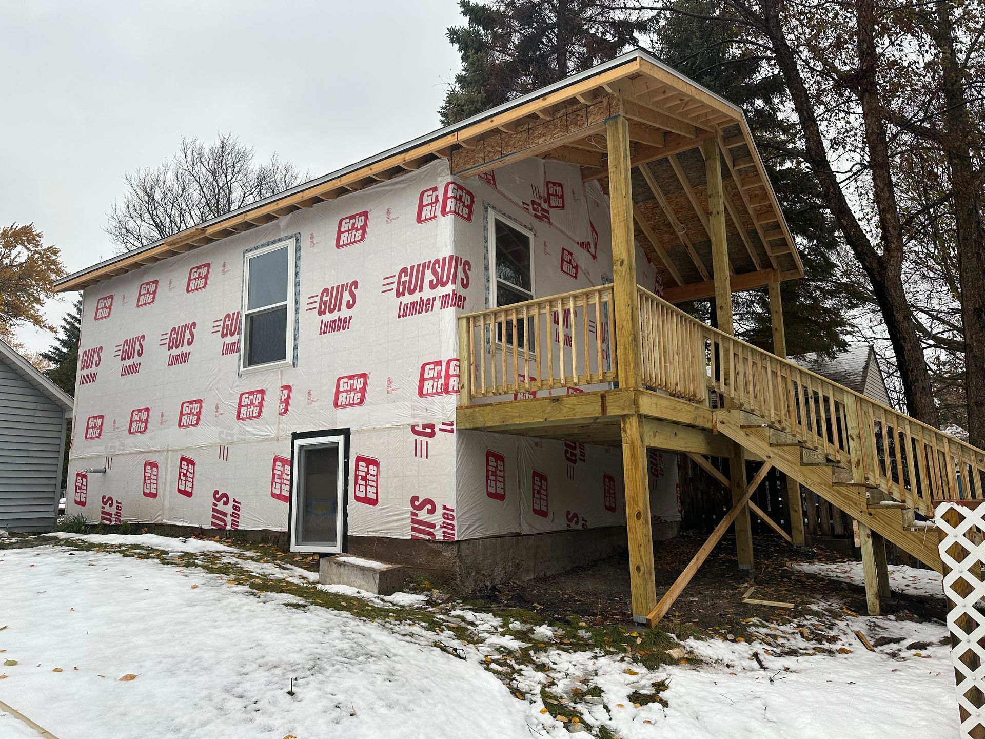A single-story house under construction, wrapped in white protective sheeting, with an unfinished wooden porch and stairs.