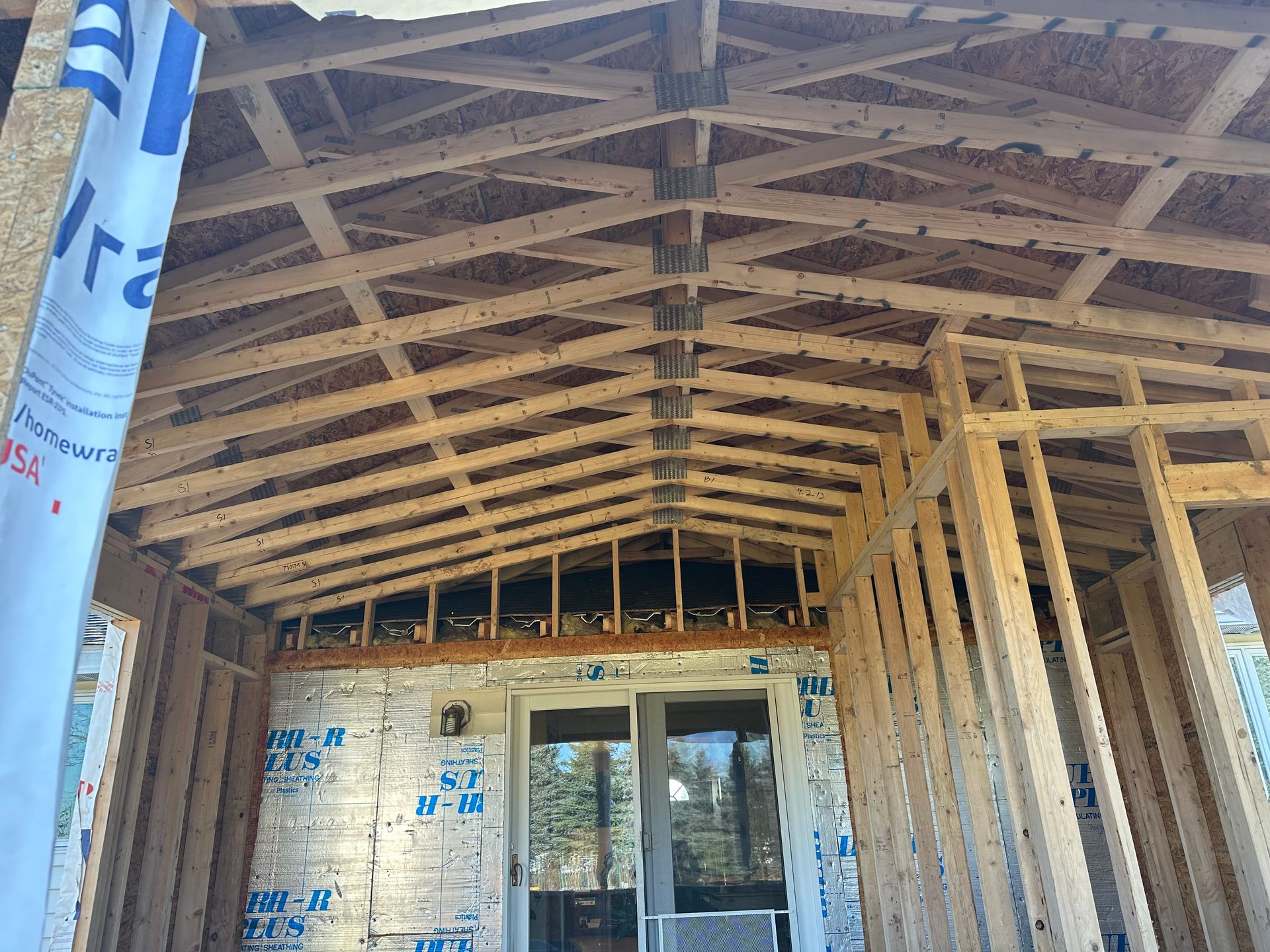 A wood-framed ceiling with a pitched roof design under construction, showing rafters, plywood, and exposed wall studs.