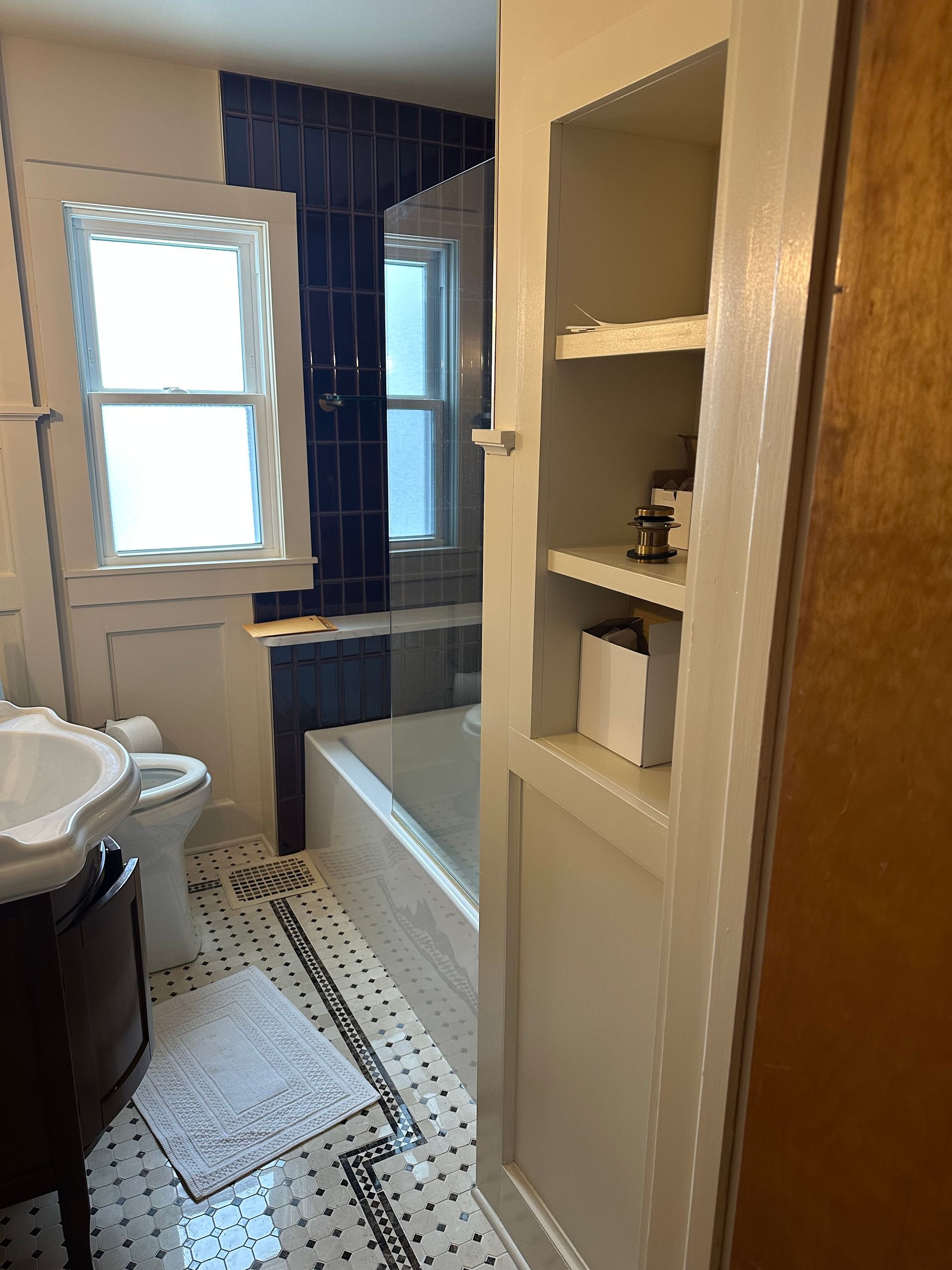 A bathroom featuring a white sink, toilet, tub, and a built-in wall shelf unit with a black and white tiled floor.