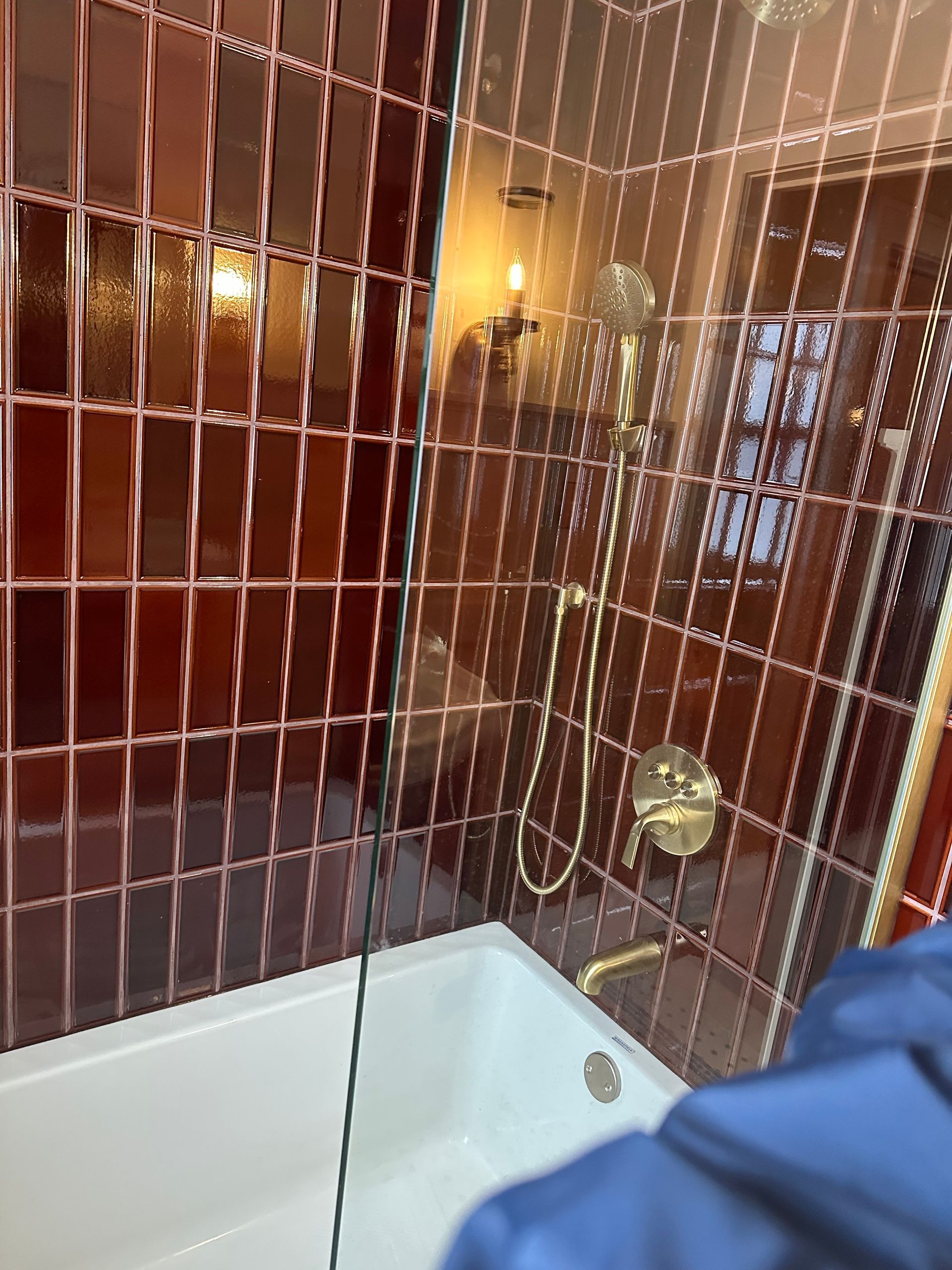 A bathtub with a gold shower fixture against a wall of deep red rectangular tiles.