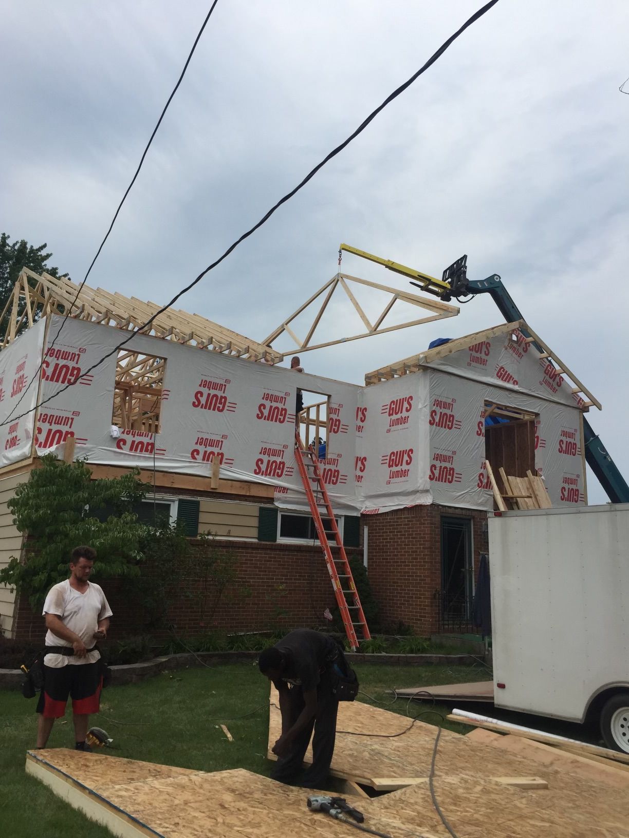 Wood-framed houses under construction on a dry field against a blue sky.