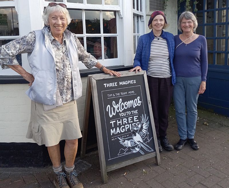 A picture of Penny, Jane, and Jean standing next to a sign at the Three Magpies pub.