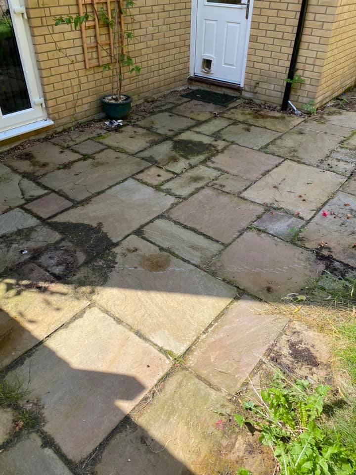 a dirty stone patio in front of a brick building, before cleaning