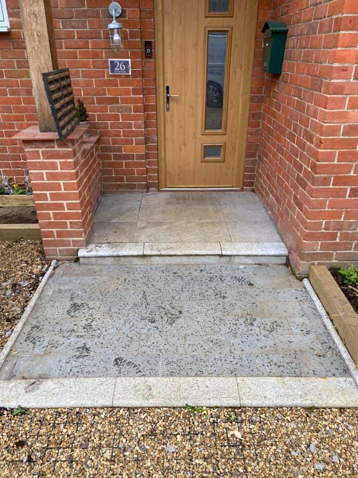 a brick house with a wooden door and a concrete walkway leading to it, before cleaning.