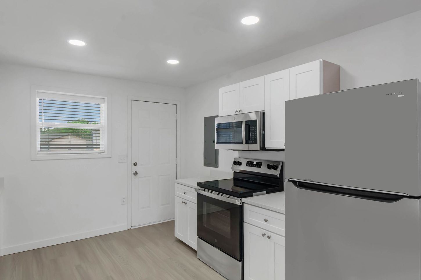 Bright white kitchen with stainless steel appliances, light wood floor, and a windowed door.