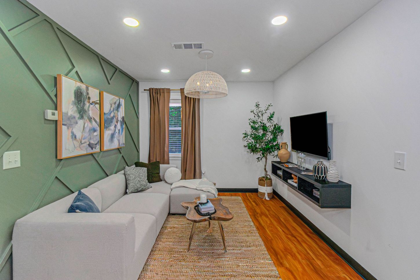 Modern living room with gray sectional, wall-mounted TV, patterned rug, and wood floor