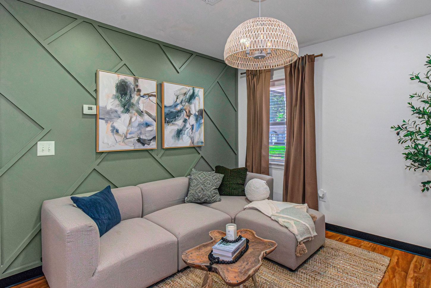 Cozy living room with a beige sectional, green accent wall, woven pendant light, and window with brown curtains