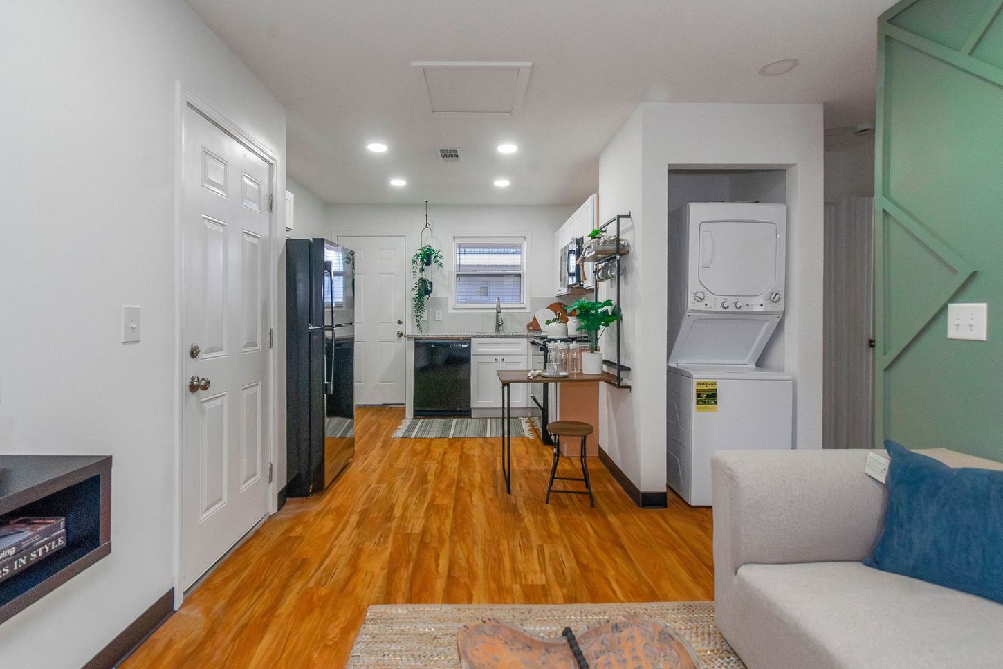 Bright open living room with wood floors, white walls, sofa, dining table, and kitchen in back