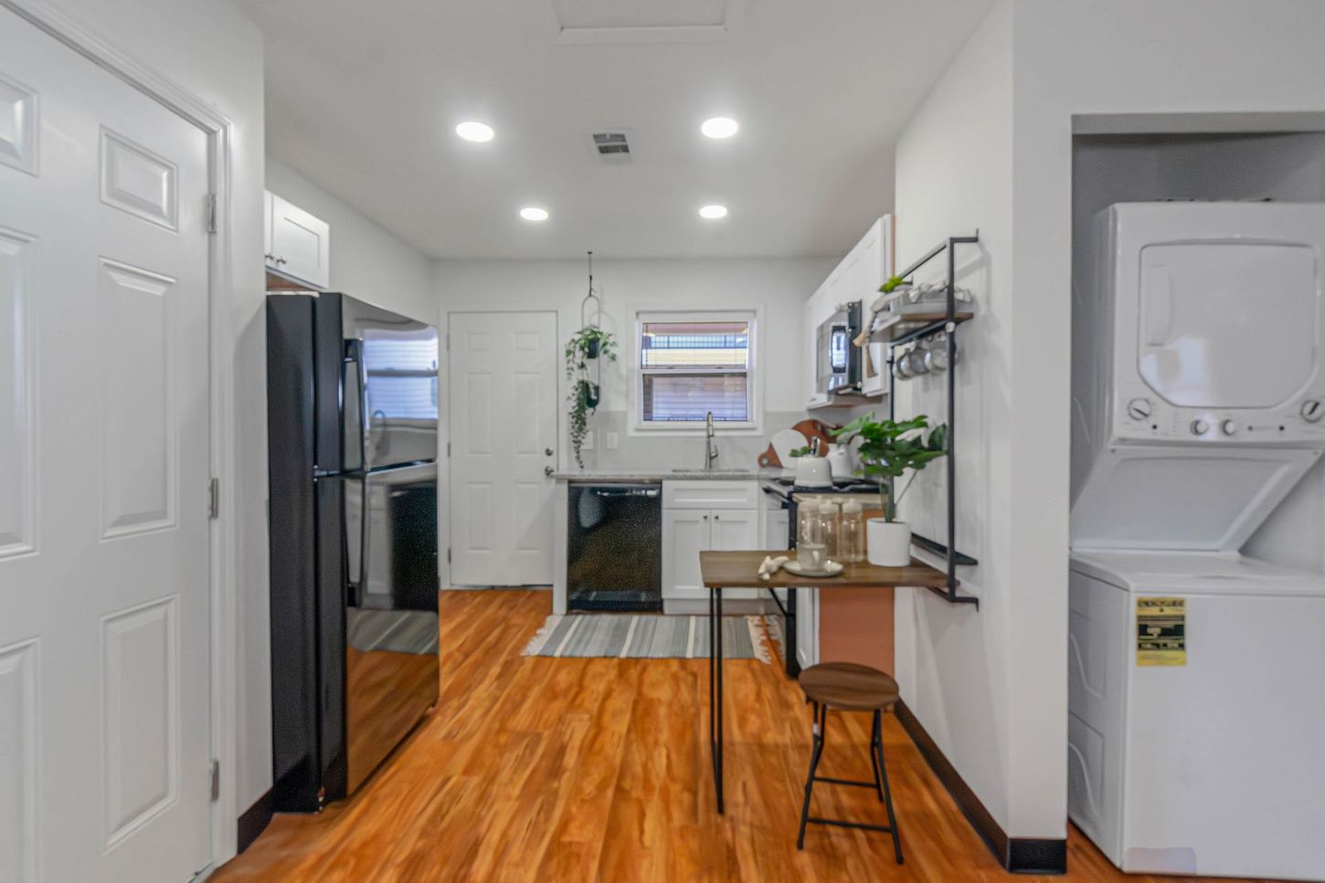 Bright kitchen with wood floor, black appliances, small island, and laundry nook on the right.