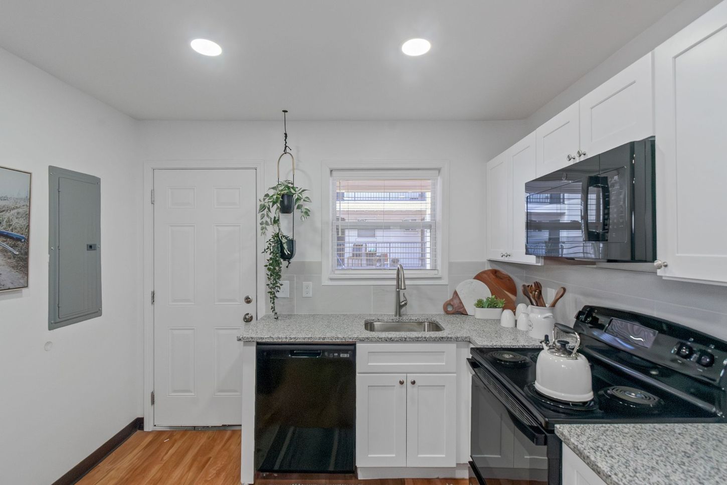 Bright white kitchen with black appliances, window over sink, and recessed ceiling lights.