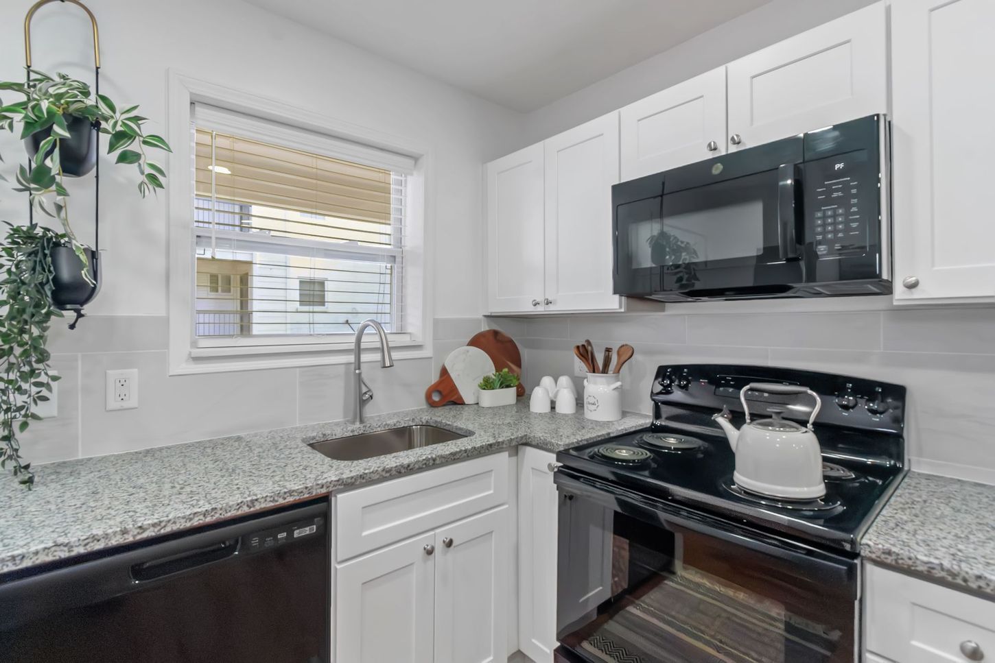 Bright kitchen with white cabinets, granite counters, black appliances, and a window over the sink
