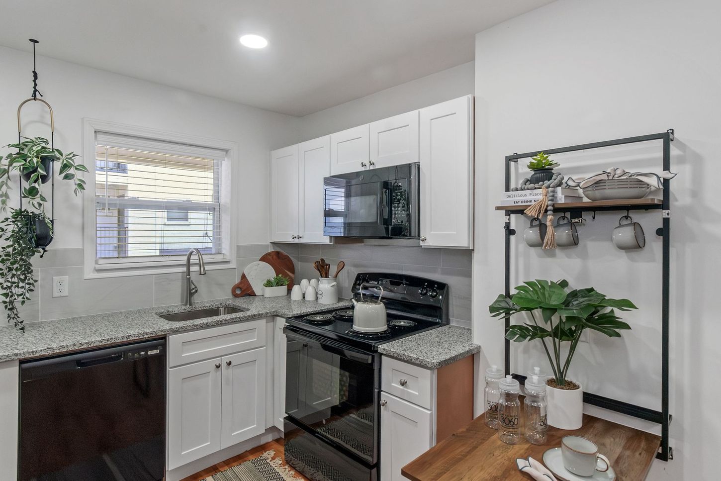 Bright white kitchen with black stove, gray countertops, and a plant on a wooden table.