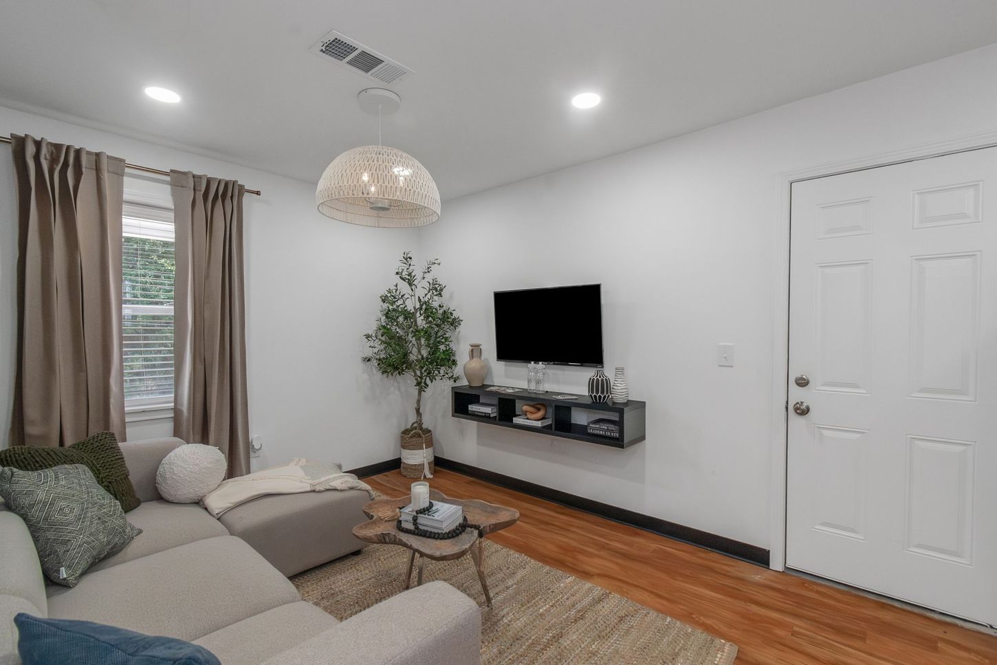 Bright living room with beige sectional, wall-mounted TV, white door, and hardwood floors