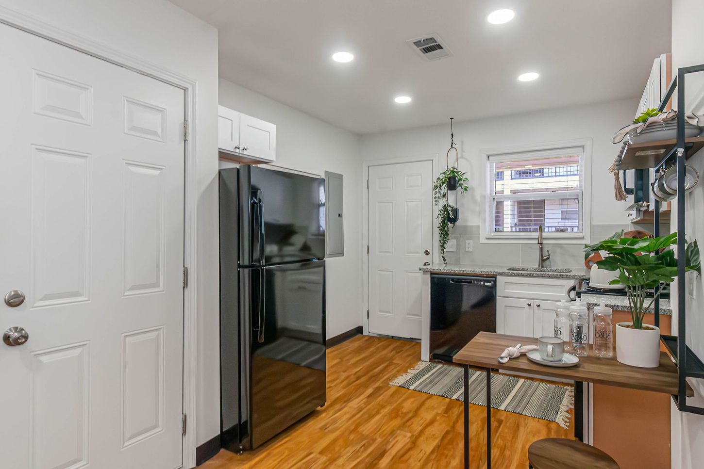 Bright kitchen with black appliances, white cabinets, wood floor, and a small table by the window