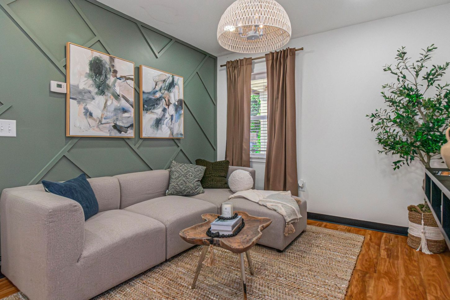 Cozy living room with gray sectional sofa, green accent wall, framed art, rug, and window with curtains.