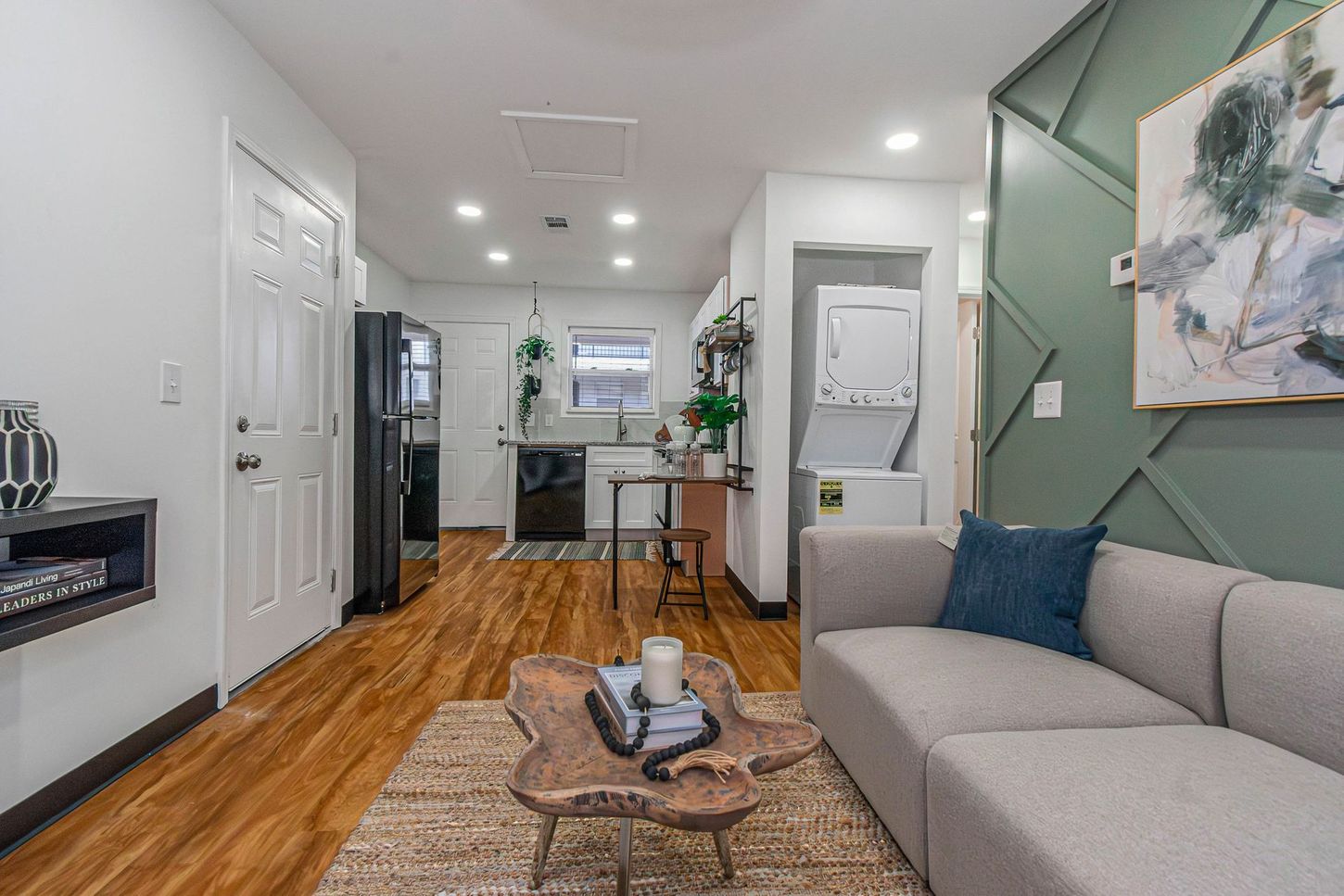 Modern living room with gray sofa, woven coffee table, patterned rug, and a hallway leading to a kitchen.